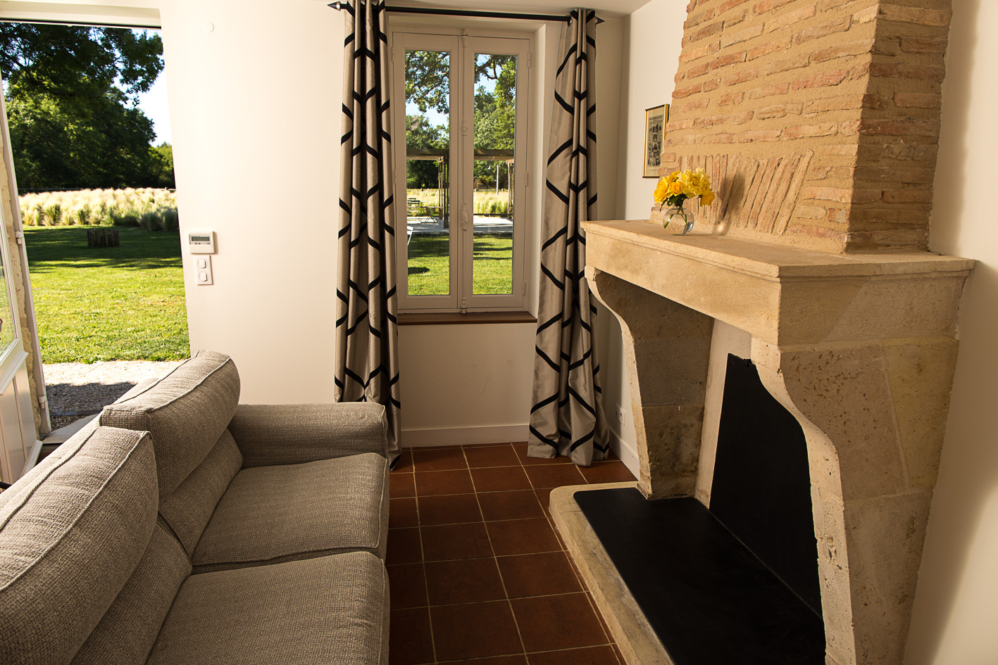 L’intérieur d’une chambre d’hôtes avec un canapé devant une cheminée et vue sur le jardin